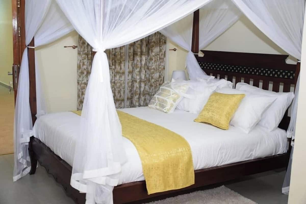 A bed with a canopy, white bedding, and a yellow throw blanket.
