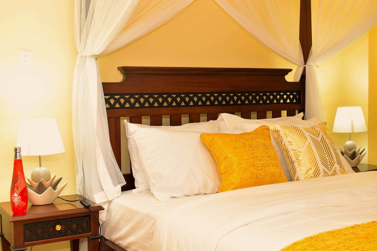 A neatly made bed with white and yellow pillows, a wooden headboard with a lattice design, and two bedside lamps on nightstands.