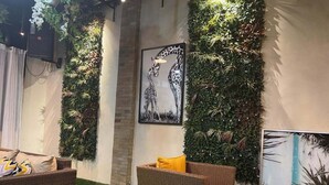 Une pièce dotée d’un sol recouvert d’un gazon synthétique vert, de meubles en osier et d’un mur décoré d’une peinture représentant une girafe et d’un mur végétal vertical.