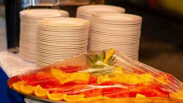 A buffet setup with stacked white plates and a covered dish with sliced fruits.