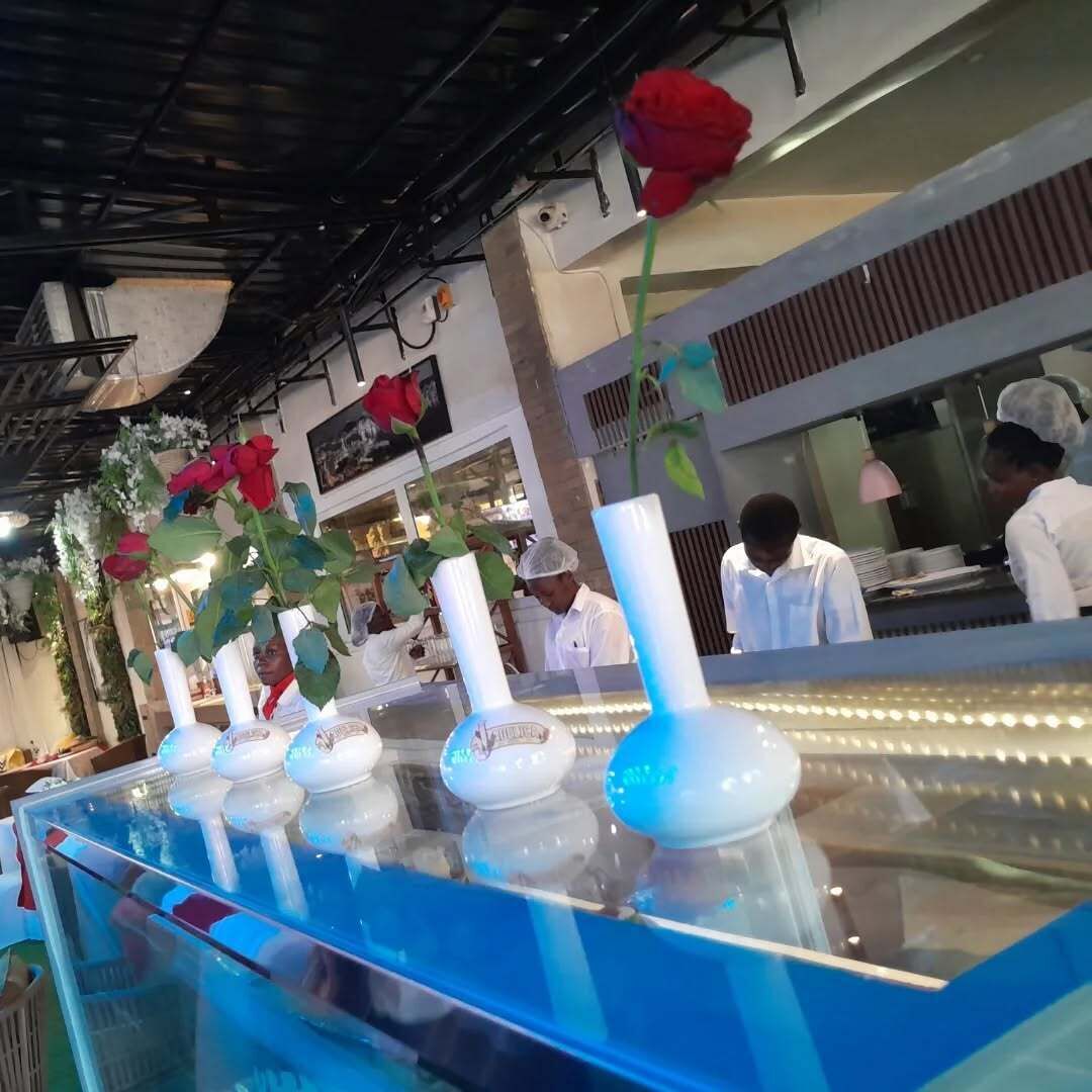 Interior de un restaurante con una barra larga, jarrones con flores y empleados con uniforme.