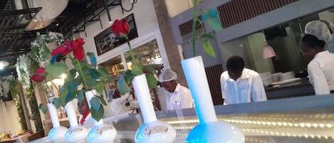 Interior de un restaurante con una barra larga, jarrones con flores y empleados con uniforme.