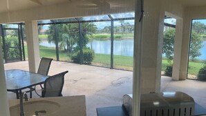 A patio area with a table and chairs, a grill, and a view of a lake and golf course.