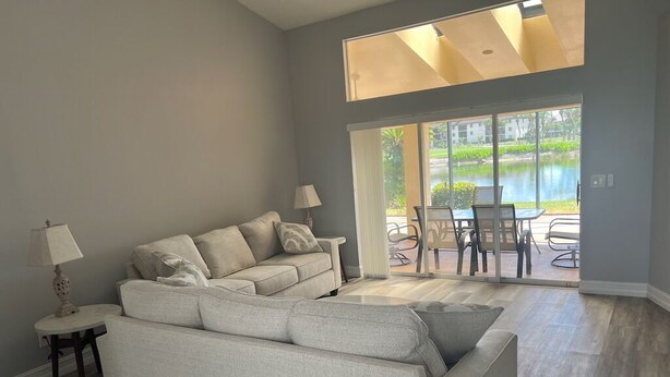 A living room with a large sofa, a small table with a lamp, and a view of a patio with outdoor furniture.