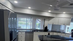 A modern kitchen with white cabinetry, a stainless steel refrigerator, and a large island with a black countertop.