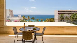 Ein Balkon mit Korbstühlen und einem Tisch, mit Blick auf Strand und Meer.
