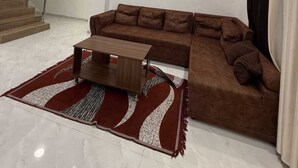 Een moderne woonkamer met een bruine modulaire bank, een houten salontafel, een tapijt met een rood-wit patroon, een plafondventilator, inbouwverlichting en een wandklok met silhouetten van vogels.