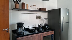 A modern kitchen with a stainless steel refrigerator, a coffee maker, a kettle, and a blender on the counter. - Apto Prédio Costa 1 c/ garagem no centro (São Roque)