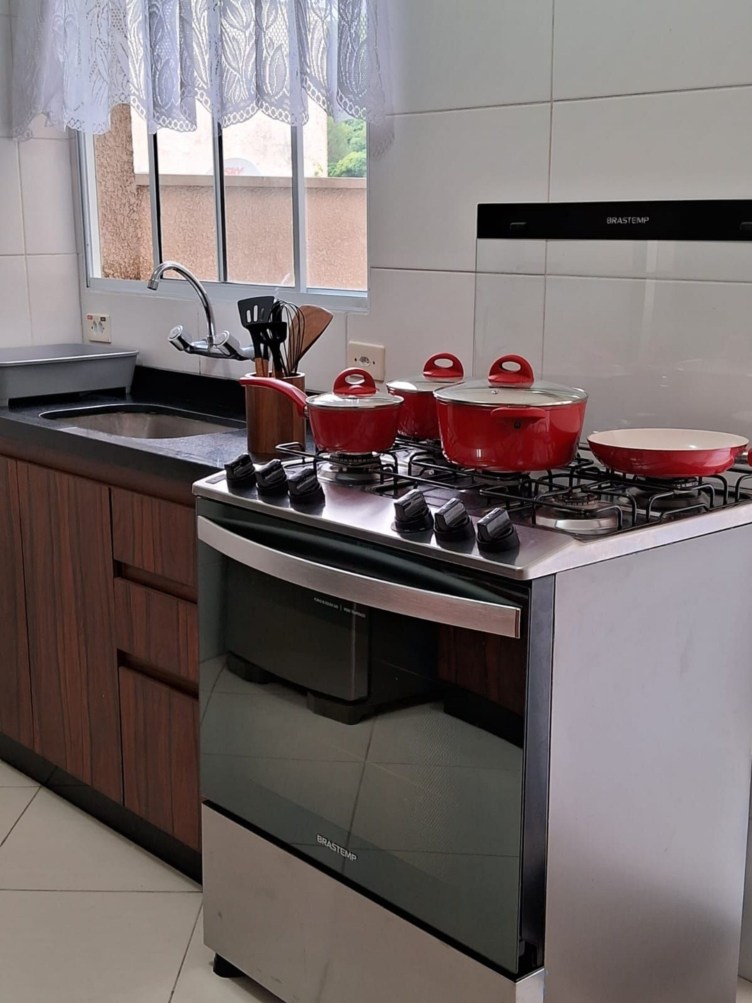 A kitchen with a stainless steel stove, red pots, a sink, and wooden cabinets.