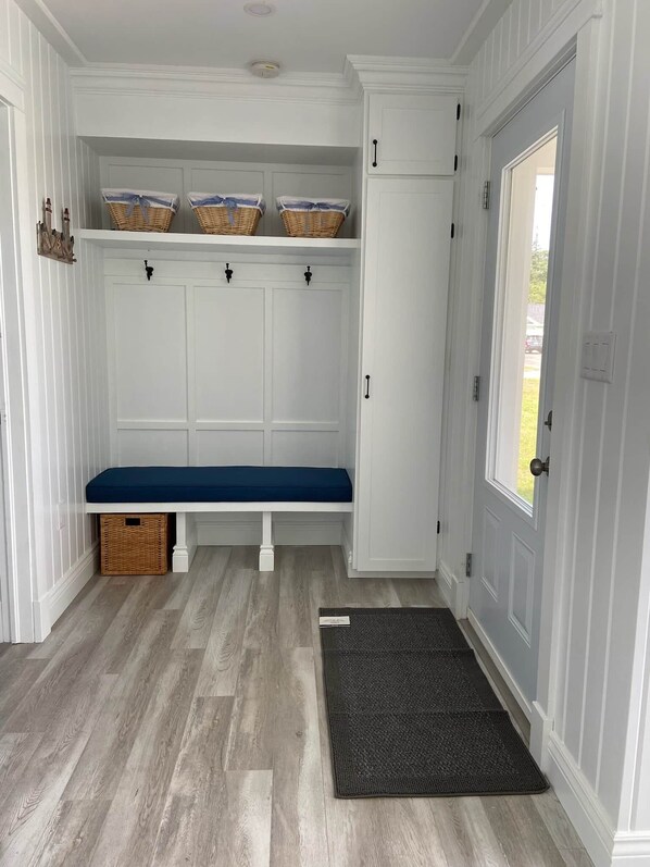 A clean, white hallway with a bench, baskets, and a door. - Blue Horizon Cottage – Steps From Private Beach, Family-Friendly Coastal Retreat (Prince Edward Island)