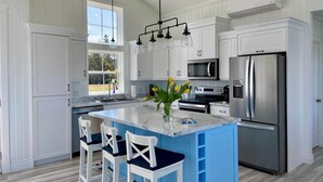 A modern kitchen with white cabinets, a central island with blue accents, stainless steel appliances, and pendant lighting. - Blue Horizon Cottage – Steps From Private Beach, Family-Friendly Coastal Retreat (Prince Edward Island)