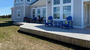 A two-story house with a covered patio area featuring outdoor furniture and a wooden deck. - Blue Horizon Cottage – Steps From Private Beach, Family-Friendly Coastal Retreat (Prince Edward Island)
