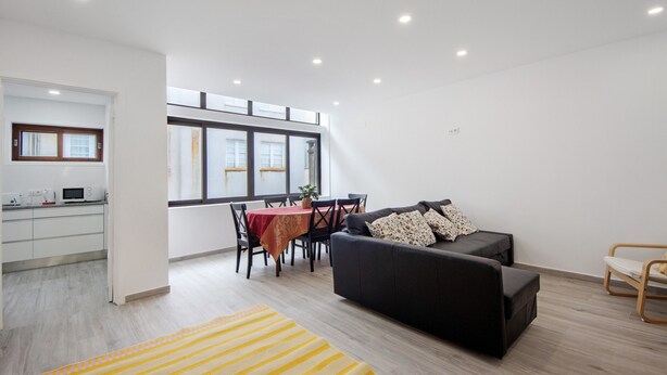 A modern living room with a black sofa, a dining table, and a kitchen area.