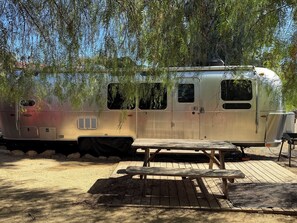 A stationary RV with a picnic table in front, surrounded by trees and rocks. - Marvelous 2-bedroom Airstream with Pool and Spa (Ojai)