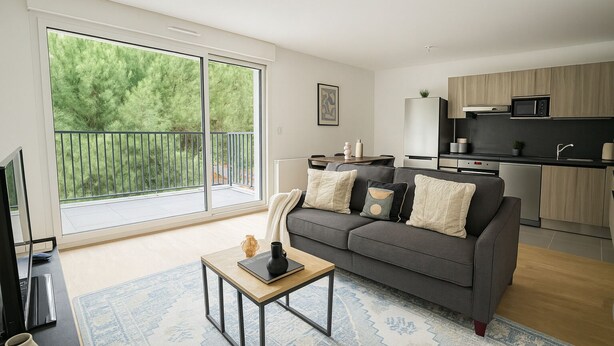 A modern living room with a grey sofa, a coffee table, and a large window overlooking a balcony.