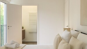 A bedroom with a large bed, a bedside table, a nightstand, and a window with blinds.