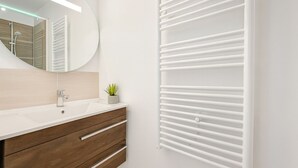 A modern bathroom with a white vanity, a round mirror, a small potted plant, and a radiator.