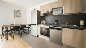 A modern kitchen with a dining area, stainless steel appliances, and light wood cabinetry.