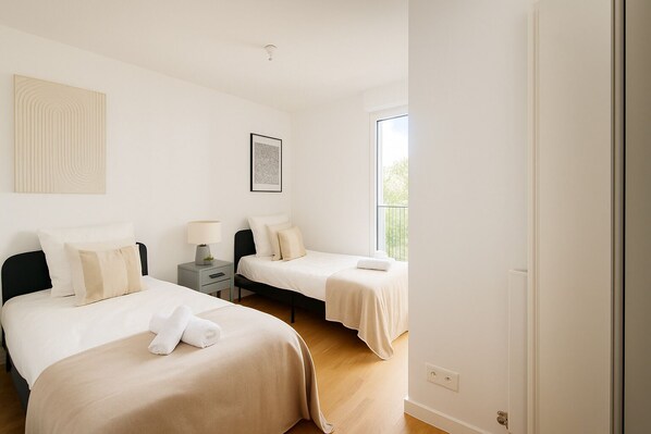 A hotel room with two beds, a bedside table with a lamp, a framed picture on the wall, and a window providing natural light. - Spacieux 3 chambres a Montrouge (Malakoff)