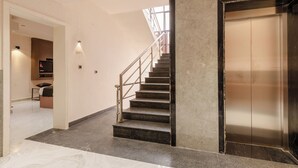 Ein modernes Interieur mit einer Marmortreppe, einer Wandleuchte und einer geschlossenen Aufzugtür.
