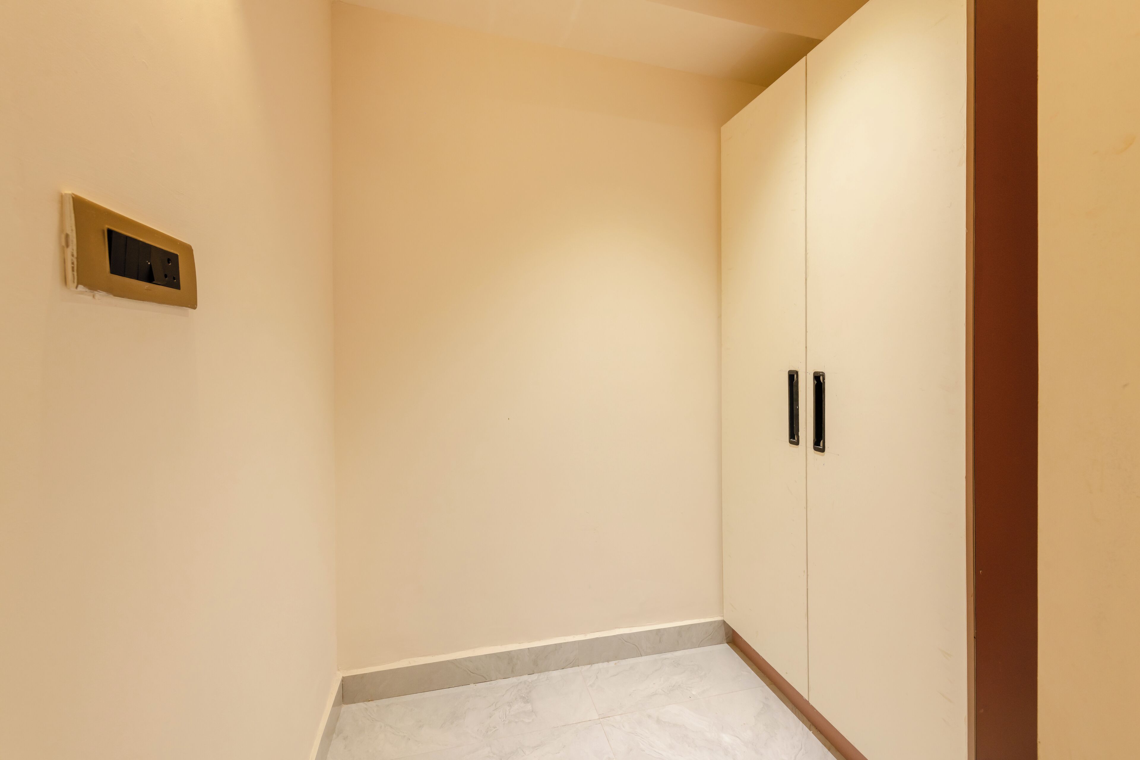 A corner of a room with a beige wall, a light switch, and a wardrobe with black handles.