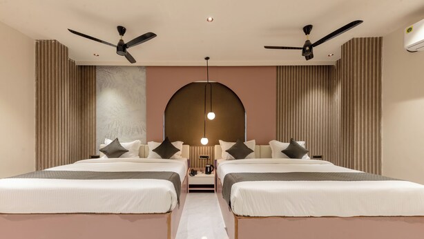Ein Hotelzimmer mit zwei Betten, Deckenventilatoren, einer zentralen Leuchte und einem großen Bogenfenster.