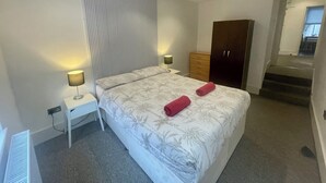 Ein Schlafzimmer mit einem Bett, zwei Nachttischlampen, einem Nachttisch, einem Kleiderschrank und einer Treppe, die zu einer oberen Etage führt.