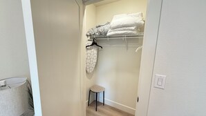 A walk-in closet with a hanging rack, a stool, and neatly folded towels. - The Sable Stay (Vancouver)