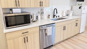 A modern kitchen with light wood cabinets, stainless steel appliances, a white countertop, and a built-in dishwasher. - The Sable Stay (Vancouver)