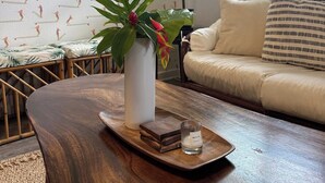 En stue med et rundt spejl, en hvid vase med en plante, et træbord og en sofa med stribede puder.