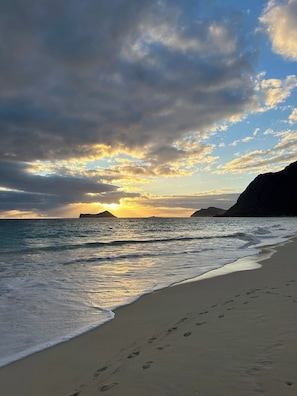 A beach with footprints leading to the water, a clear sky, and distant landforms.