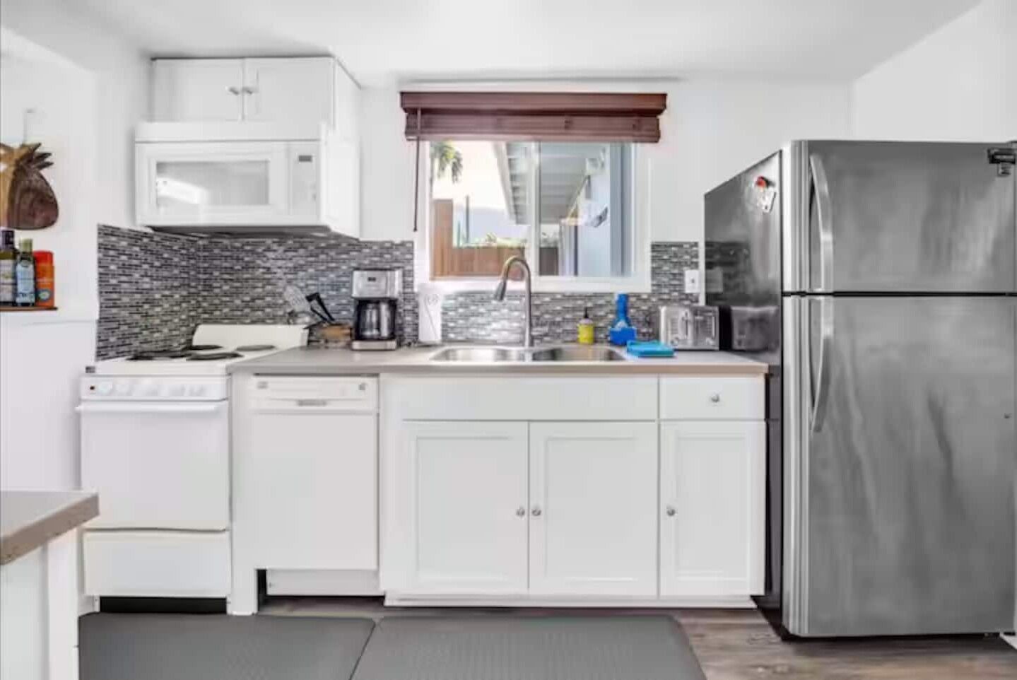 A modern kitchen with white cabinets, a stainless steel refrigerator, a microwave, and a coffee maker.