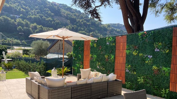 Une terrasse avec un ensemble de meubles de jardin en osier, un parasol et une table à plateau en verre.