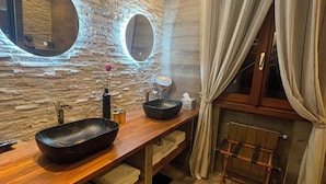 Une salle de bain avec un meuble-lavabo en bois, deux miroirs ronds, un lavabo noir et un porte-serviettes.