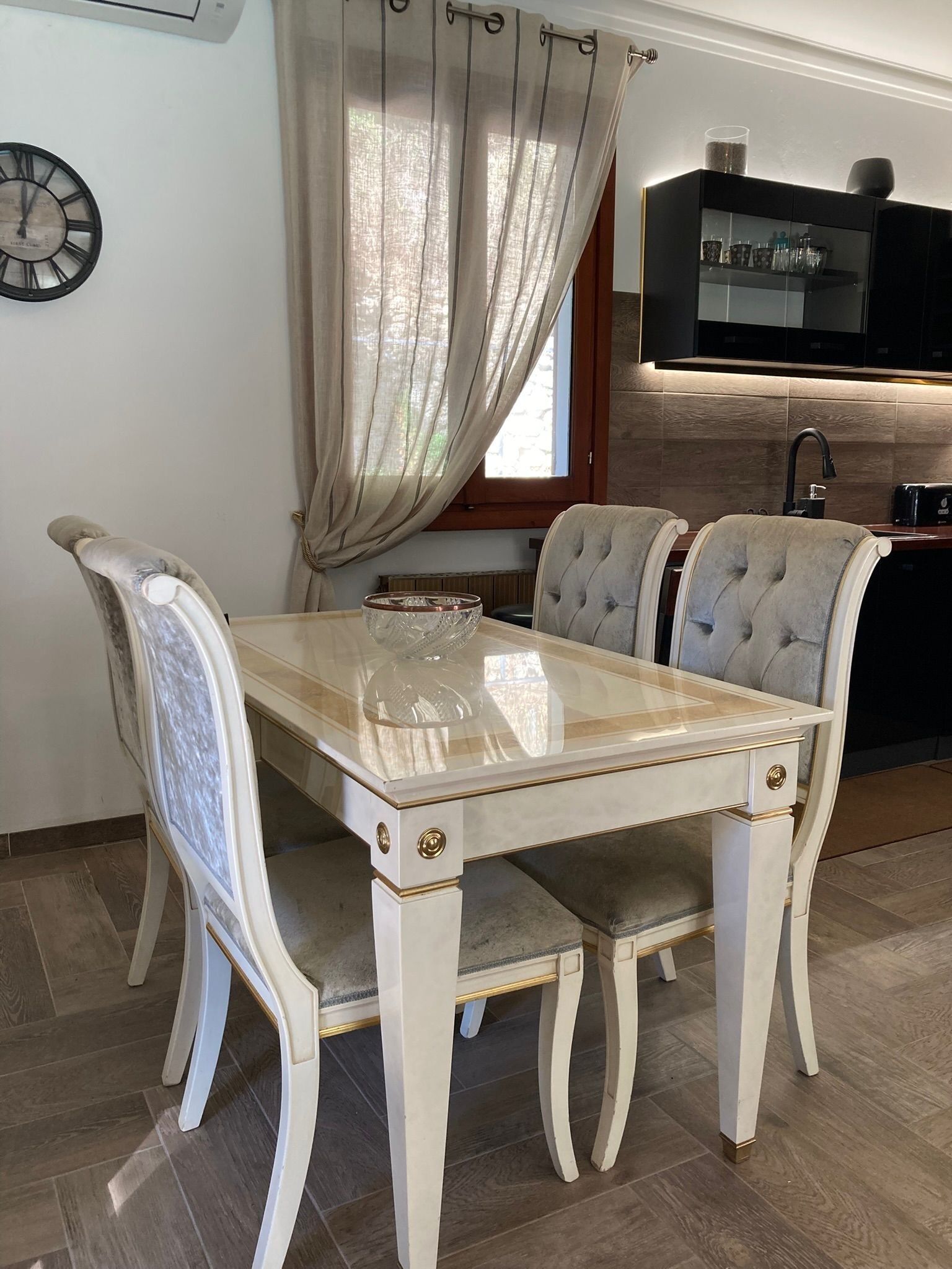 A dining table with four chairs, a glass-top table, and a clock on the wall.