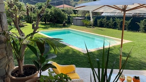 Une piscine entourée d’une pelouse bien entretenue, avec un parasol blanc et une chaise en osier à proximité.