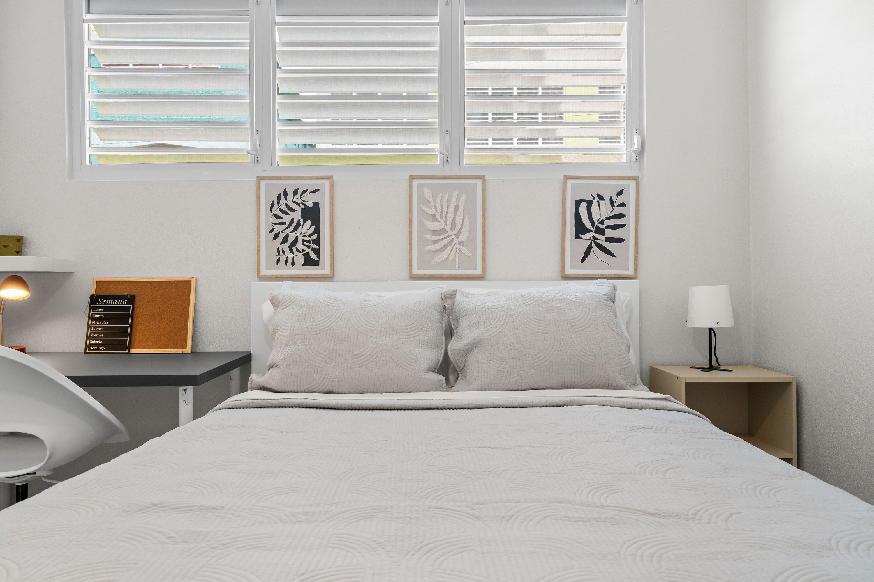 Un dormitorio con cama, mesita de noche, una silla y una obra de arte en la pared.