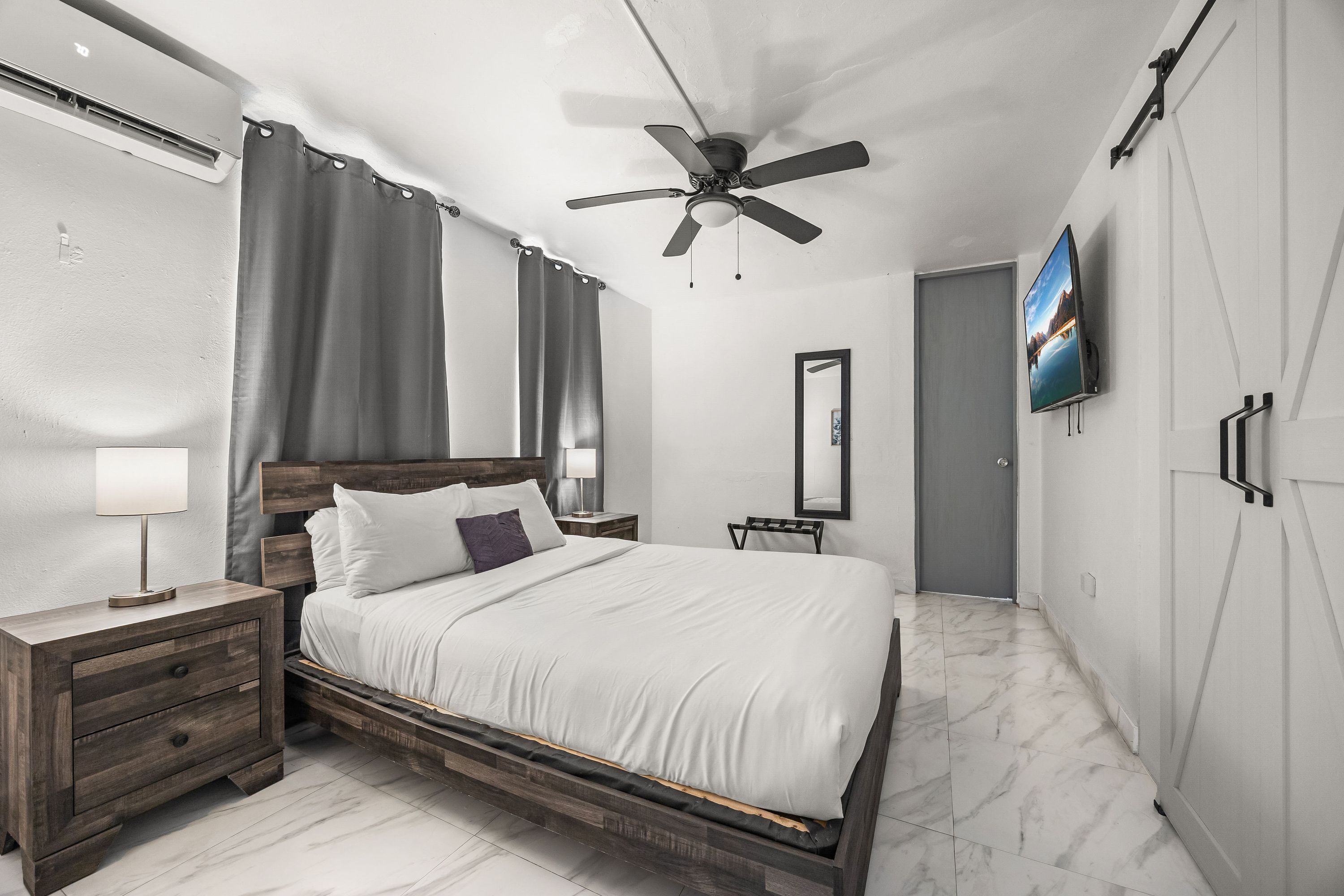 Un dormitorio moderno con estructura de cama de madera, ventilador de techo, televisor de pantalla plana y un espejo grande.