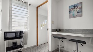 Eine moderne Küche mit Mikrowelle, Kaffeemaschine und einer kleinen Ablagefläche. Zwei Barhocker und ein Bild hängen an der Wand.