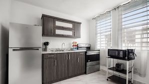 Eine moderne Küche mit Kühlschrank, Mikrowelle, Toaster und Kaffeemaschine auf einem Wagen, Holzschränken und einem Fenster mit Vorhängen.
