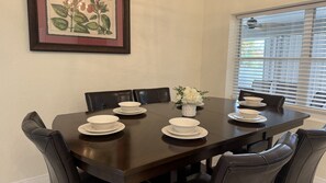 A dining table with white plates and bowls, black chairs, a vase with flowers, and a framed botanical illustration on the wall.