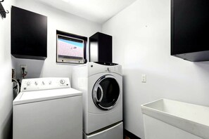 Ein Waschraum mit einer Frontlader-Waschmaschine und einem Trockner, einem kleinen Fenster mit Aussicht und einem an der Wand montierten Fernseher.