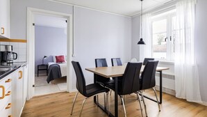 A modern kitchen with a dining area, a bed, and a window with curtains. - Bright & Spacious Getaway (Marmaverken)