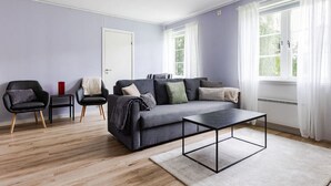 A modern living room with a grey sofa, two armchairs, a coffee table, and a door. - Bright & Spacious Getaway (Marmaverken)