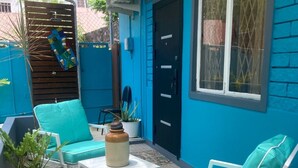 A blue-painted outdoor patio with white furniture, including two chairs and a table, surrounded by potted plants. - Welcome to The Studio Nest — your peaceful perch in paradise. (Diego Martin)