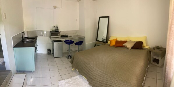 Una habitación de hotel compacta con una cama, un pequeño rincón americano, un escritorio y un espejo.