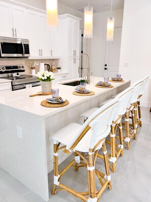 A modern kitchen with white cabinetry, stainless steel appliances, and a central island with bar stools. - “Stylish Cape Coral Villa with Private Pool, Sunshine & Serenity!” (Cape Coral)