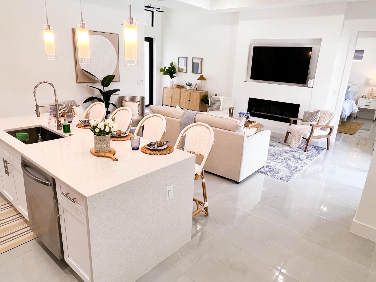 A modern kitchen with a central island, dining area with chairs, a sofa, a TV, and a fireplace.