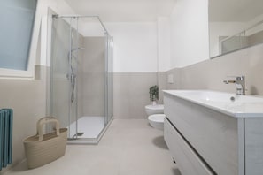 Un baño moderno con cabina de ducha de vidrio, un lavabo blanco y un inodoro.