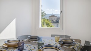 Een eettafel met kommen en glazen, een raam met uitzicht op een gebouw en bomen, en een deur.